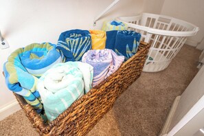 Een rieten mand gevuld met kleurrijke dekens en een witte babybed in de achtergrond.