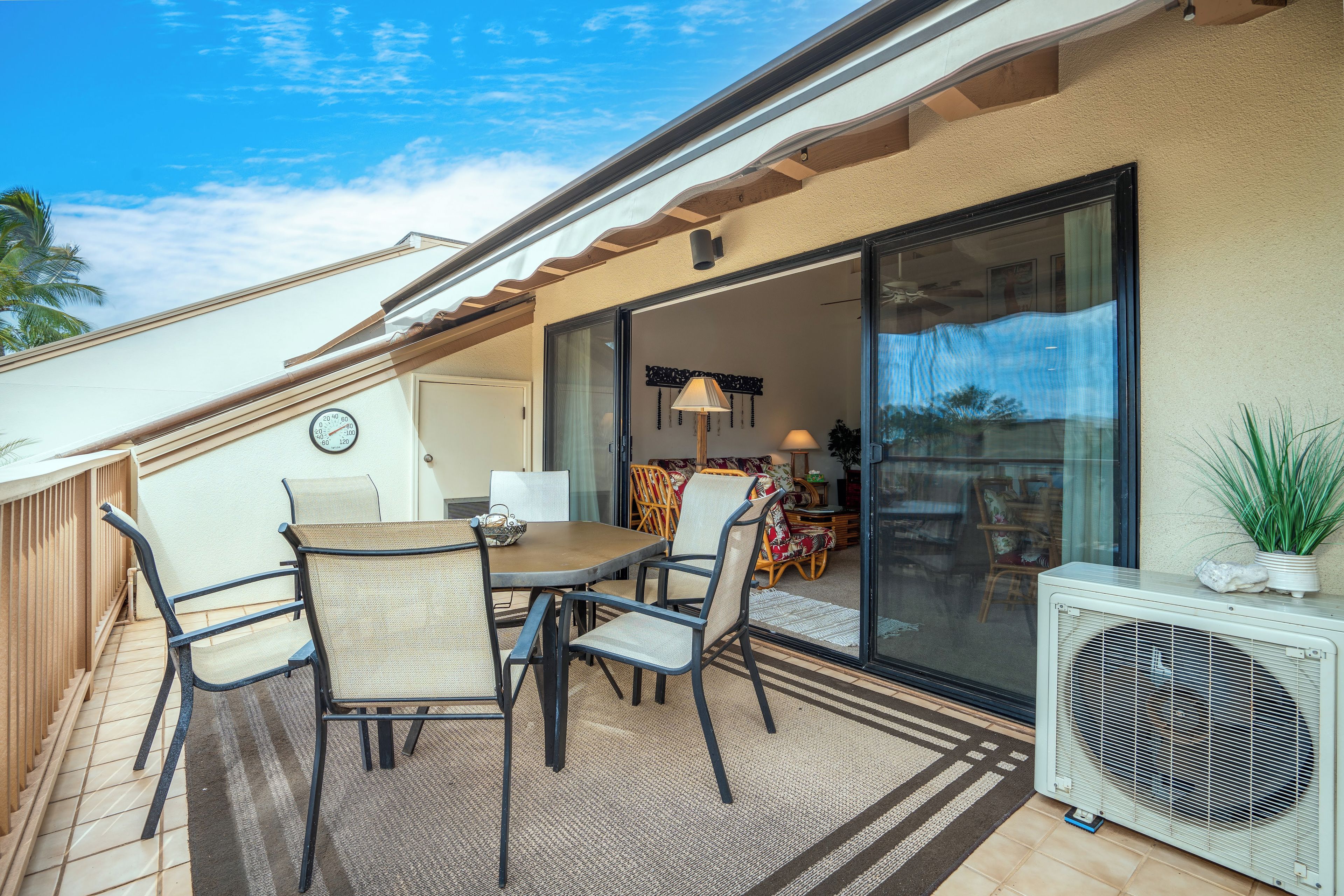 Une terrasse couverte avec une table et des chaises, une porte-fenêtre coulissante donnant sur un espace intérieur et un appareil de climatisation.