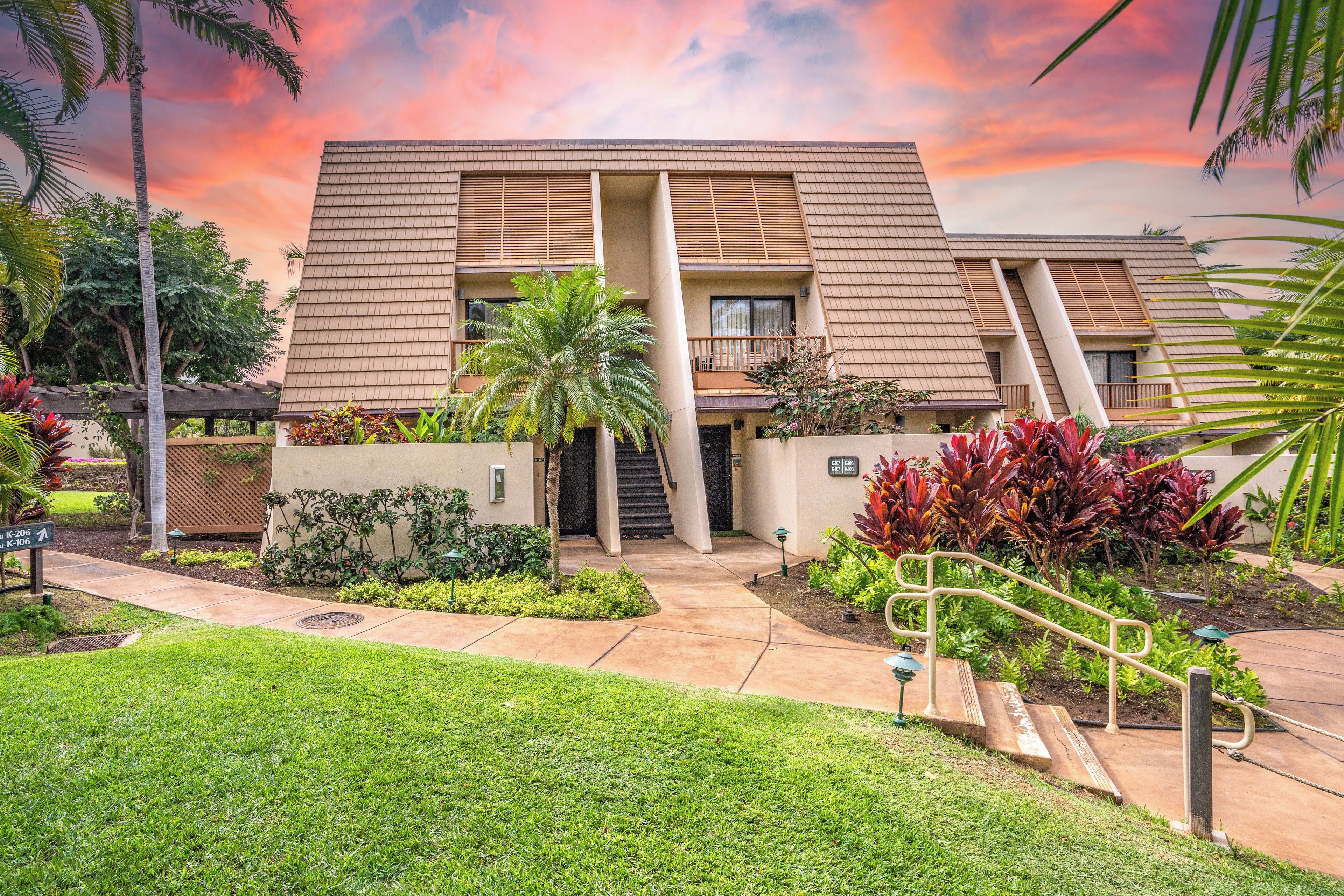 A modern building with a flat roof, a central staircase, and a well-maintained garden with various plants and a palm tree.