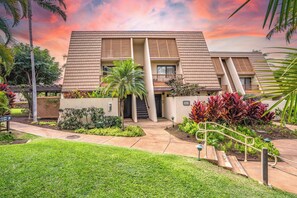 A modern building with a flat roof, a central staircase, and a well-maintained garden with various plants and a palm tree.