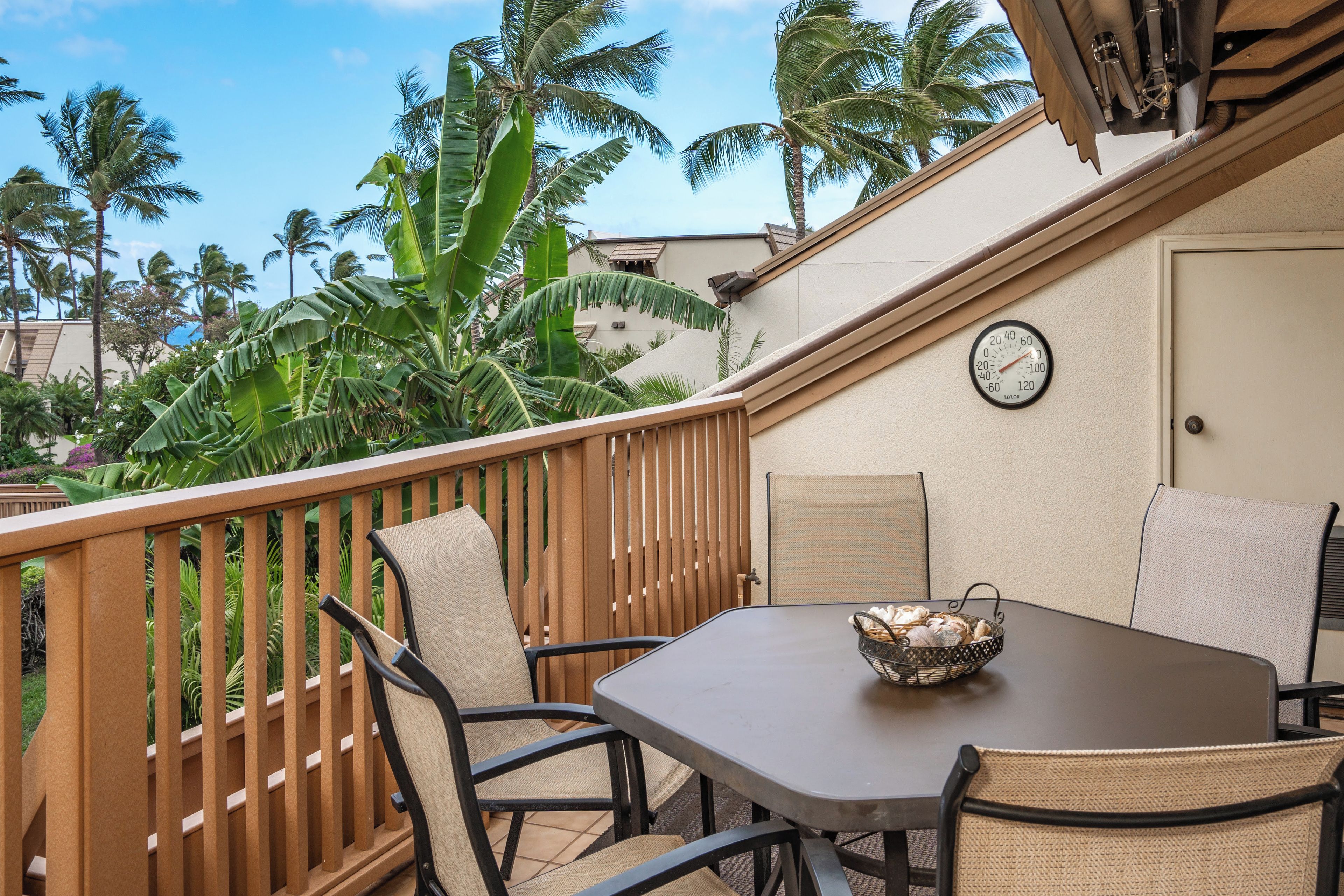 A patio with a table and chairs, surrounded by a wooden fence and palm trees.