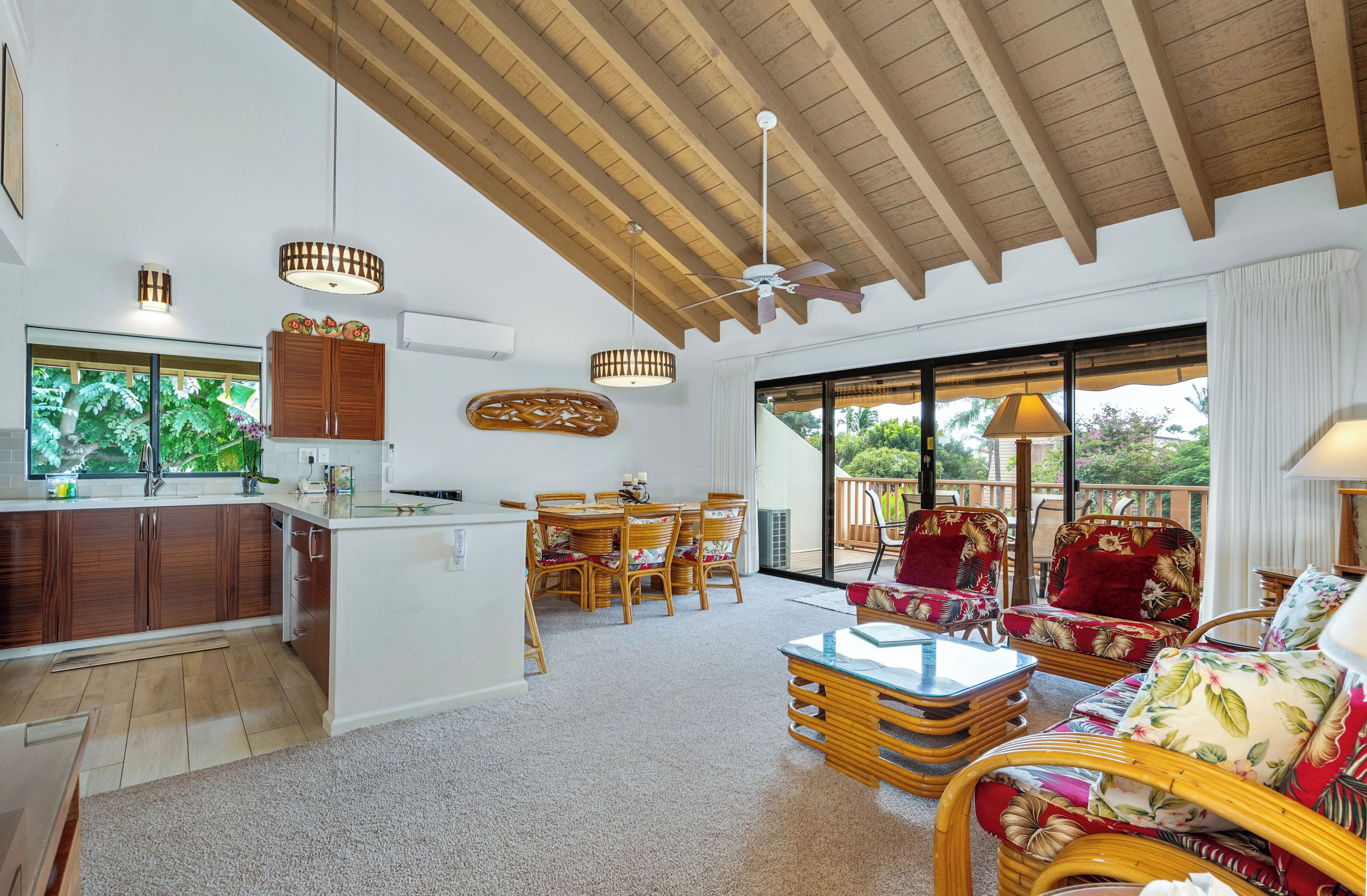 A spacious living area with a wooden ceiling, a dining set, and a view through large sliding doors to an outdoor deck.