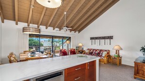 A spacious kitchen with a large island, wooden ceiling beams, and a view of the outdoors. - Maui Kamaole K-207 Recently Remodeled, Views, Pools, Hot Tub, A/C, W/D (Kihei)