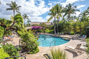 A pool area with lounge chairs, palm trees, and a building in the background. - Maui Kamaole K-207 Recently Remodeled, Views, Pools, Hot Tub, A/C, W/D (Kihei)