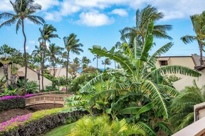 Un jardin tropical avec des palmiers, un pont en bois et un bâtiment à la façade beige.