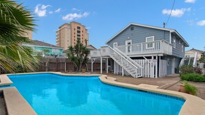 A swimming pool with a wooden deck and stairs leading to a house.