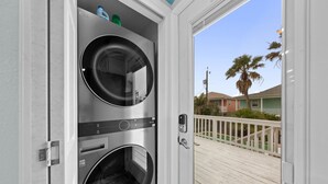 A laundry room with two stacked washing machines and a view of a wooden deck and palm trees outside.