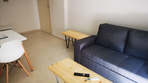 A living room with a grey sofa, a white chair, and two wooden tables. - City Center Apartment Project 3 by Cretan Houses (Heraklion)