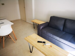 Un salon avec un canapé gris, un fauteuil blanc et deux tables en bois.