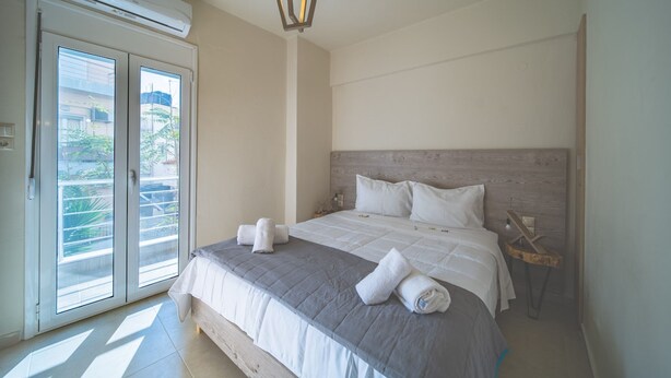 A bedroom with a bed, a wooden headboard, a nightstand, and a window with a view of greenery. - City Center Apartment Project 3 by Cretan Houses (Heraklion)