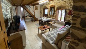 A rustic interior with a stone wall, wooden beams, a dining area, and a sofa.