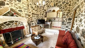 A stone-walled room with a fireplace, a sofa, a striped rug, and a television.