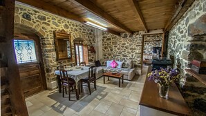 A rustic stone-walled room with a wooden ceiling, a dining table with chairs, a sofa, and a small table with a vase of flowers.