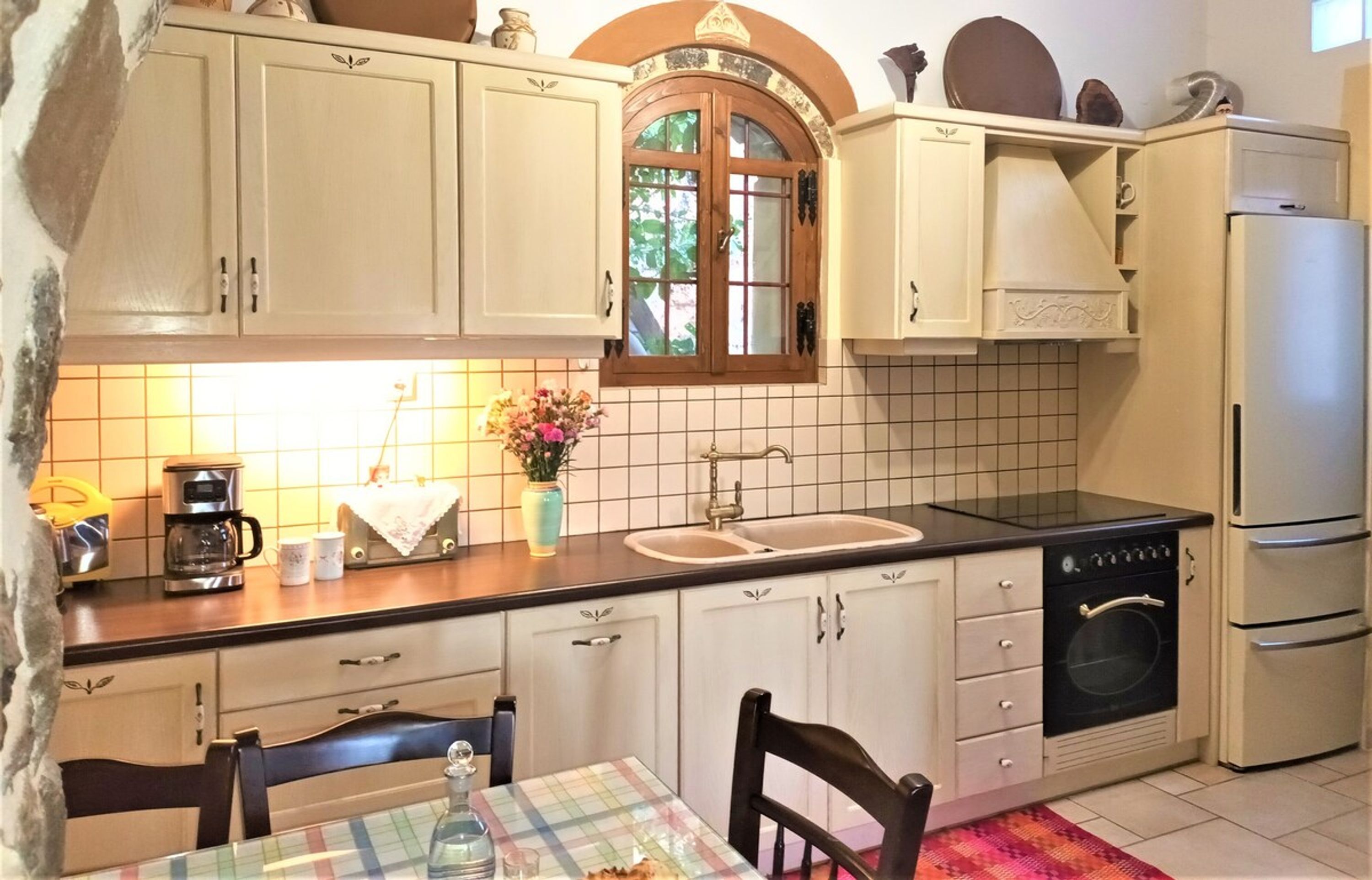 Une cuisine avec des meubles blancs, une cuisinière noire, un évier et une fenêtre donnant sur un paysage verdoyant.