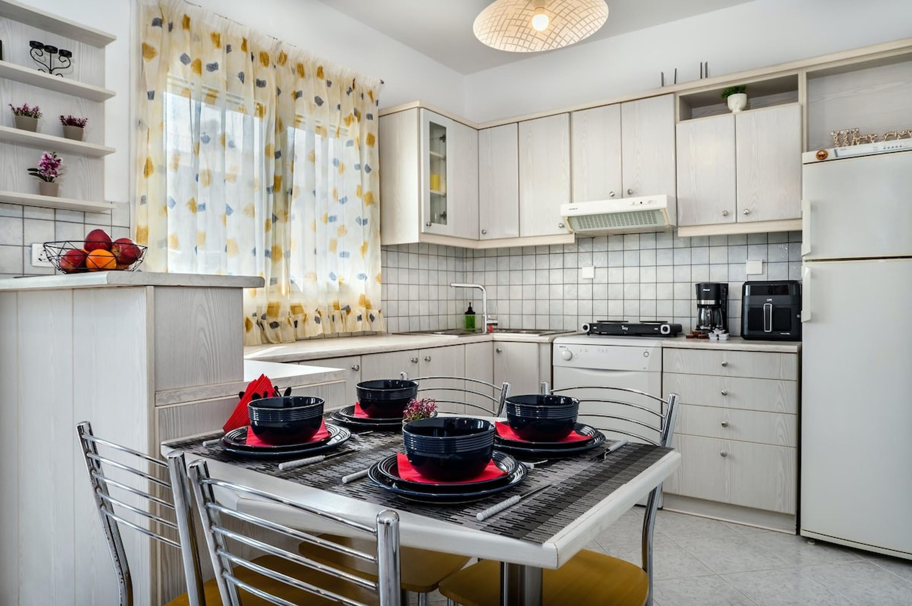 A modern kitchen with white cabinets, a dining table set with black bowls and red plates, and a coffee maker.