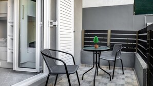 En balkon med to stole og et bord, en skydedør i glas og en lille plantepotte.