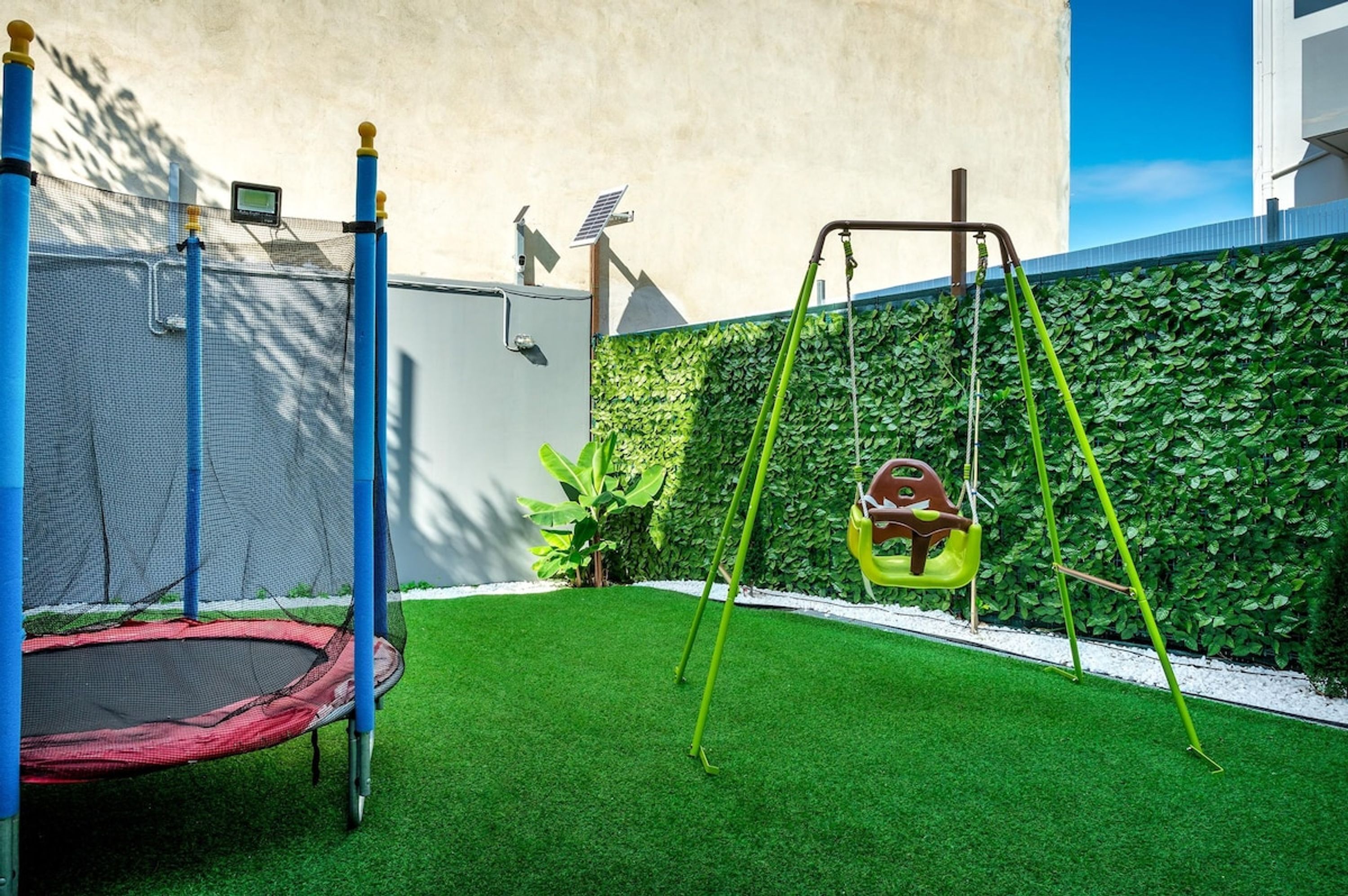 A backyard with a trampoline, swings, and a green artificial turf.