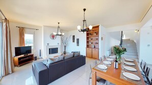 A modern living room with a sofa, TV, fireplace, and dining area set for a meal. - Villa Angelika Two-storey House With Pool for 7 (Hersonissos)