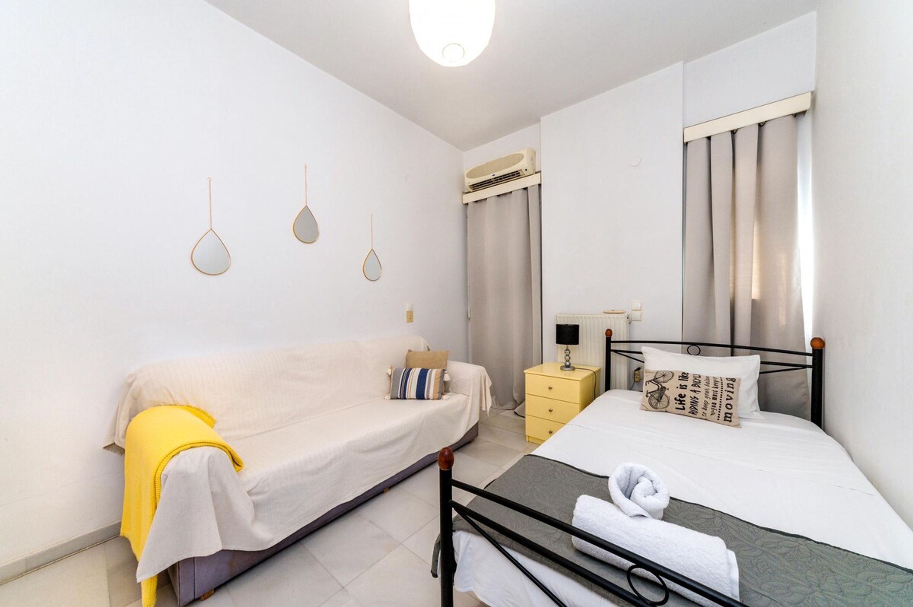Un dormitorio con cama, mesita de noche, lámpara, aire acondicionado instalado en la pared y una ventana con cortinas.