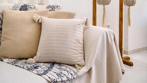 A bedroom with a bed, pillows, a macrame plant hanger, and a window with sheer curtains.