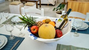 A dining table set with a fruit bowl, wine bottle, and glasses.