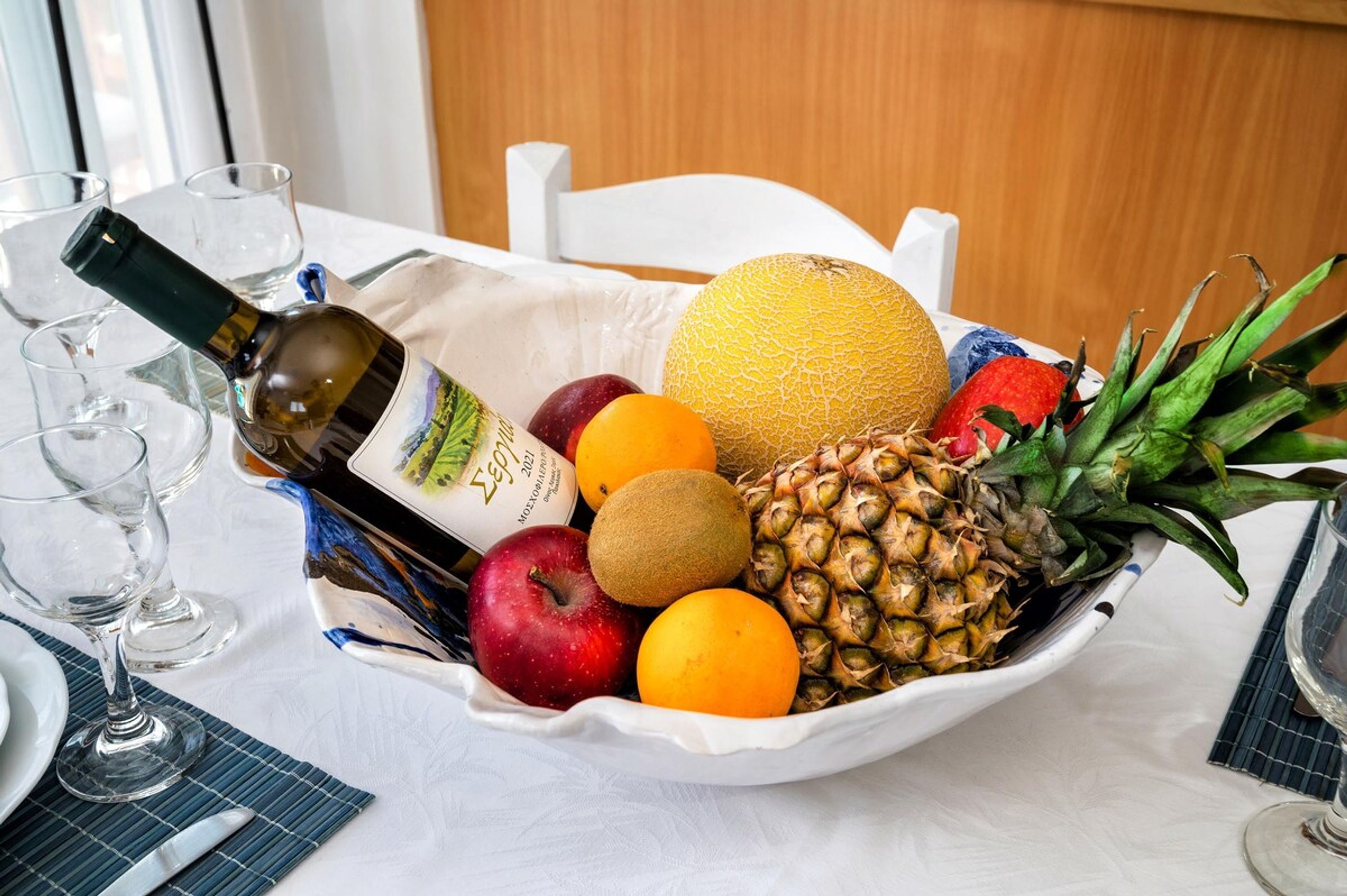 A fruit bowl with a bottle and glasses on a table.