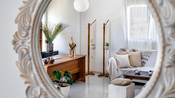 A modern living room with a wooden desk, a sofa, and a coffee table. There are plants and decorative items on the desk and sofa.