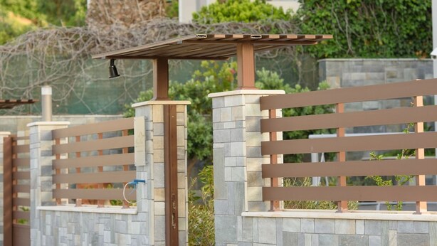 A gated entrance with a palm tree, stone walls, and a pergola. - Marie Nicol Apartments 2 (Malevizi)
