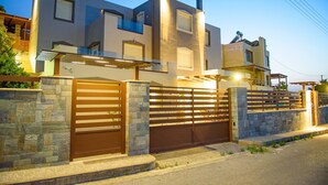 A modern two-story house with a stone wall and a wooden gate. - Marie Nicol Apartments 2 (Malevizi)