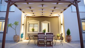 An outdoor patio with a pergola, two wooden chairs, a table, and potted plants. - Marie Nicol Apartments 2 (Malevizi)