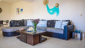 A modern living room with a grey sectional sofa, striped pillows, a coffee table with decorative items, and a wall-mounted hat. - Marie Nicol Apartments 2 (Malevizi)