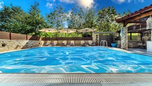 A swimming pool with lounge chairs and umbrellas, surrounded by trees and a stone wall. - Villa Kalouas Private Pool (Malevizi)