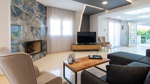 A modern living room with a fireplace, a large flat-screen TV, and comfortable seating. - Marie Nicol Apartments Private Pool 3 Bedrooms (Malevizi)