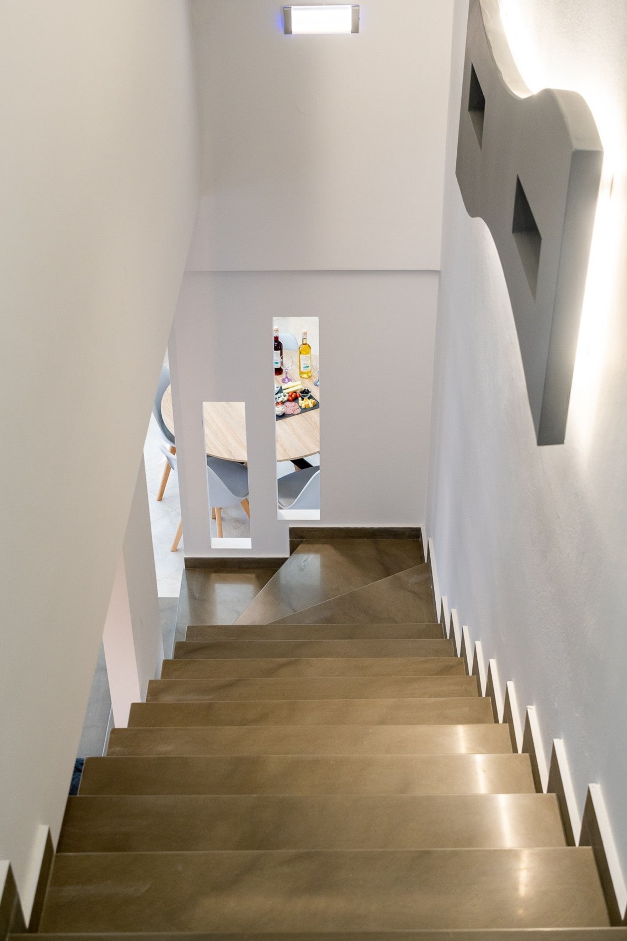A staircase with a modern design, leading to a room with a dining area.