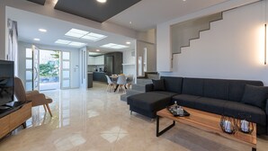 A modern living room with a sofa, coffee table, and TV. There is a staircase and a kitchen in the background. - Marie Nicol Apartments Private Pool 3 Bedrooms (Malevizi)