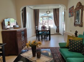Una sala de estar con un sofá verde, un mueble de madera, una mesa de comedor con sillas y un ventanal con cortinas.