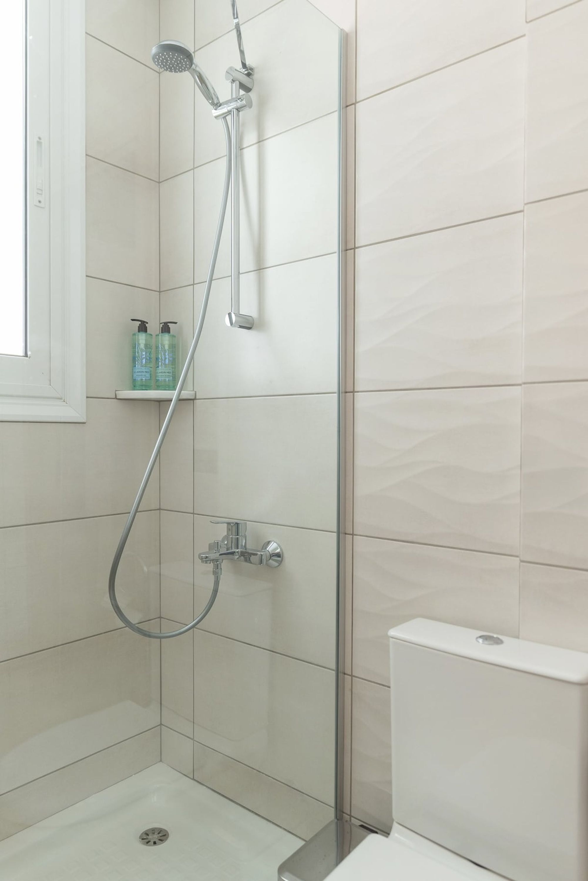 A modern shower area with a glass door, a handheld showerhead, and a wall-mounted faucet.