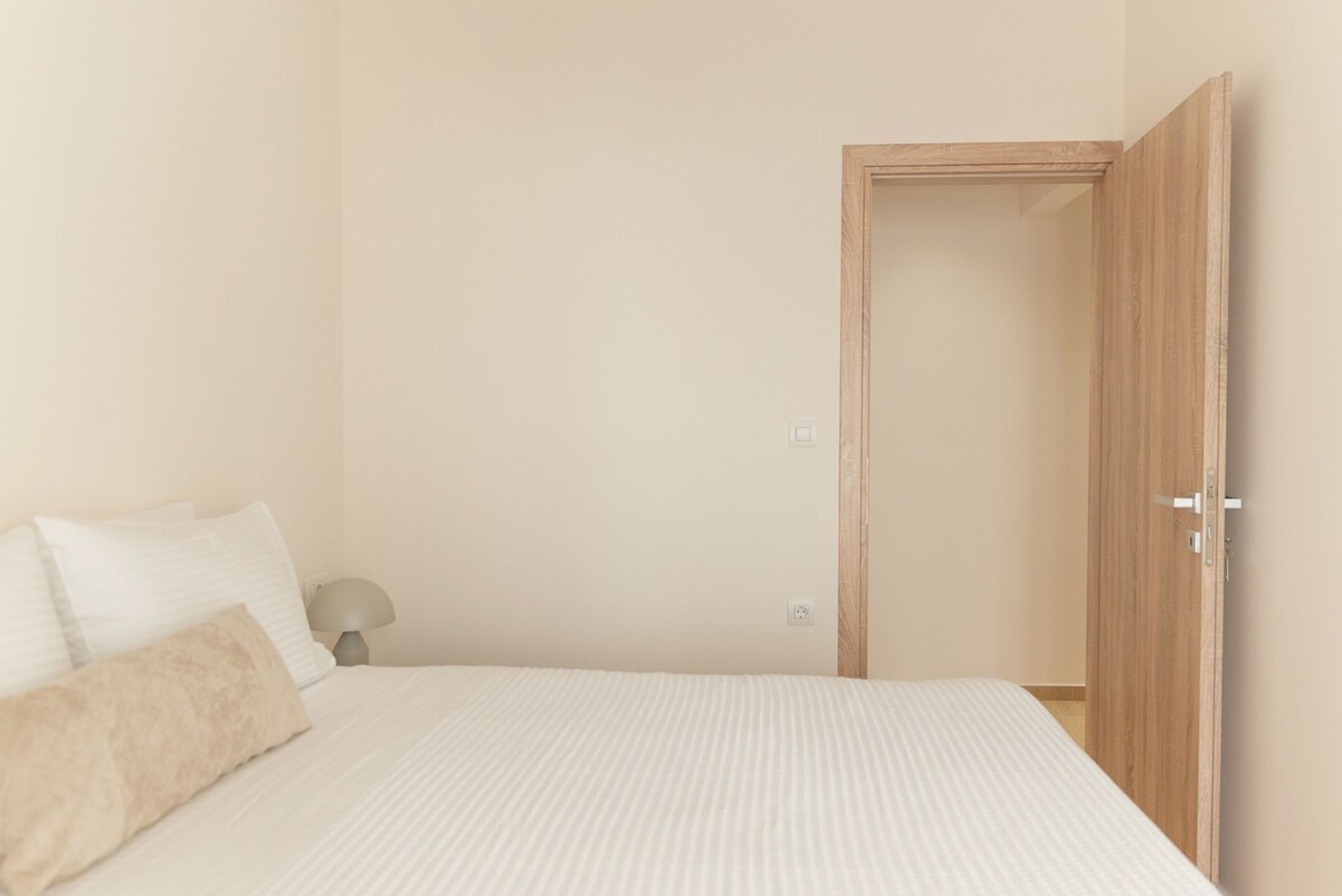 Ein Schlafzimmer mit Bett, Kissen, einem Nachttisch und einer Holztür.