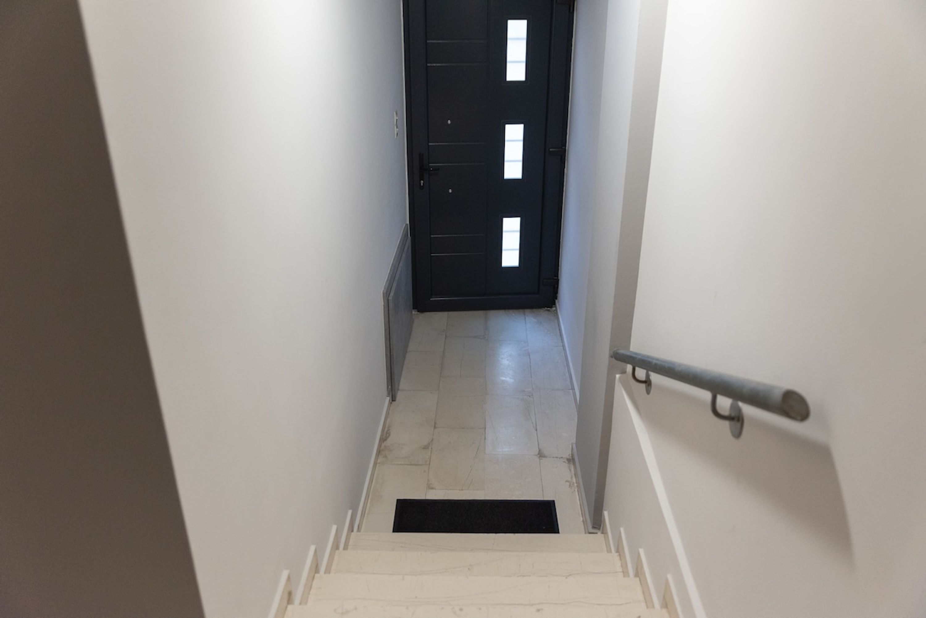 A narrow stairway leading to a dark door with a metal handrail.