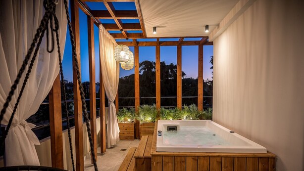 Una terraza de madera con un jacuzzi, bancos de madera y una silla colgante.