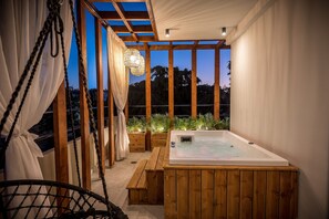 Une terrasse en bois avec un jacuzzi, des bancs en bois et une chaise suspendue.