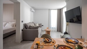 Una habitación de hotel moderna con cama, sofá, mesa de comedor con desayuno y televisor montado en la pared.