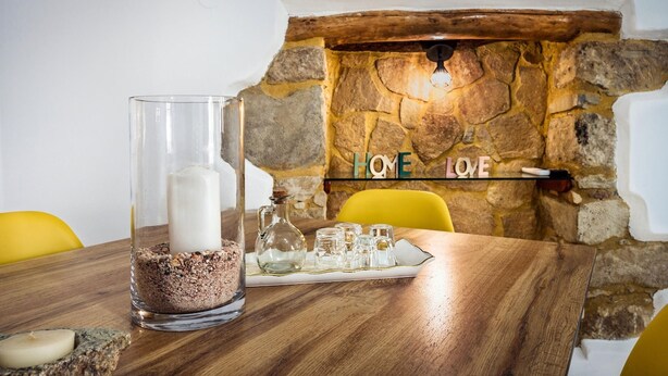 A dining table with a candle in a glass holder, a tray with glasses and a pitcher, and a stone wall with the words "HOME LOVE" in the background. - Mela s Home Agioi Deka (Gortyna)