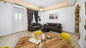 A modern living room with two sofas, a dining table, and a stone accent wall. - Mela s Home Agioi Deka (Gortyna)