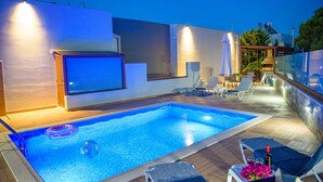 A modern outdoor pool area with a wooden deck, lounge chairs, and a glass balustrade. - Villa Marie Nicol Private Pool (Malevizi)