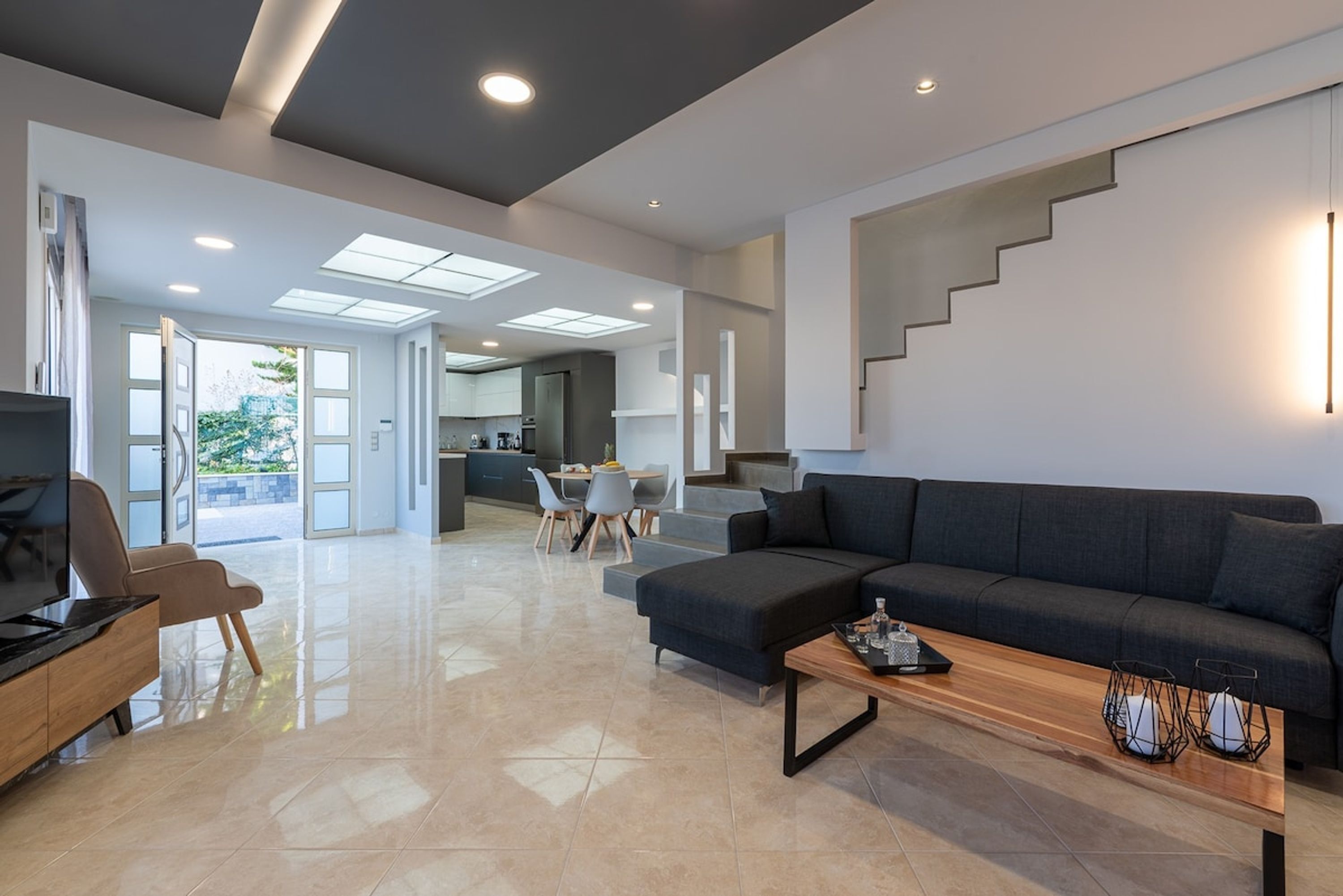 A spacious living area with a dark sofa, a wooden coffee table, and a TV on a wooden stand. A staircase leads to an upper level.