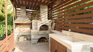 An outdoor kitchen area with a stone-built pizza oven, a sink, and a wooden cabinet. - Villa Marie Nicol Private Pool (Malevizi)