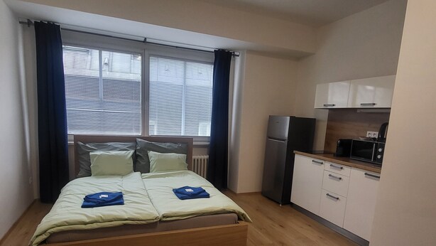 Ein kleines Zimmer mit einem Bett, einer Küchenzeile und einem Fenster mit Jalousien.