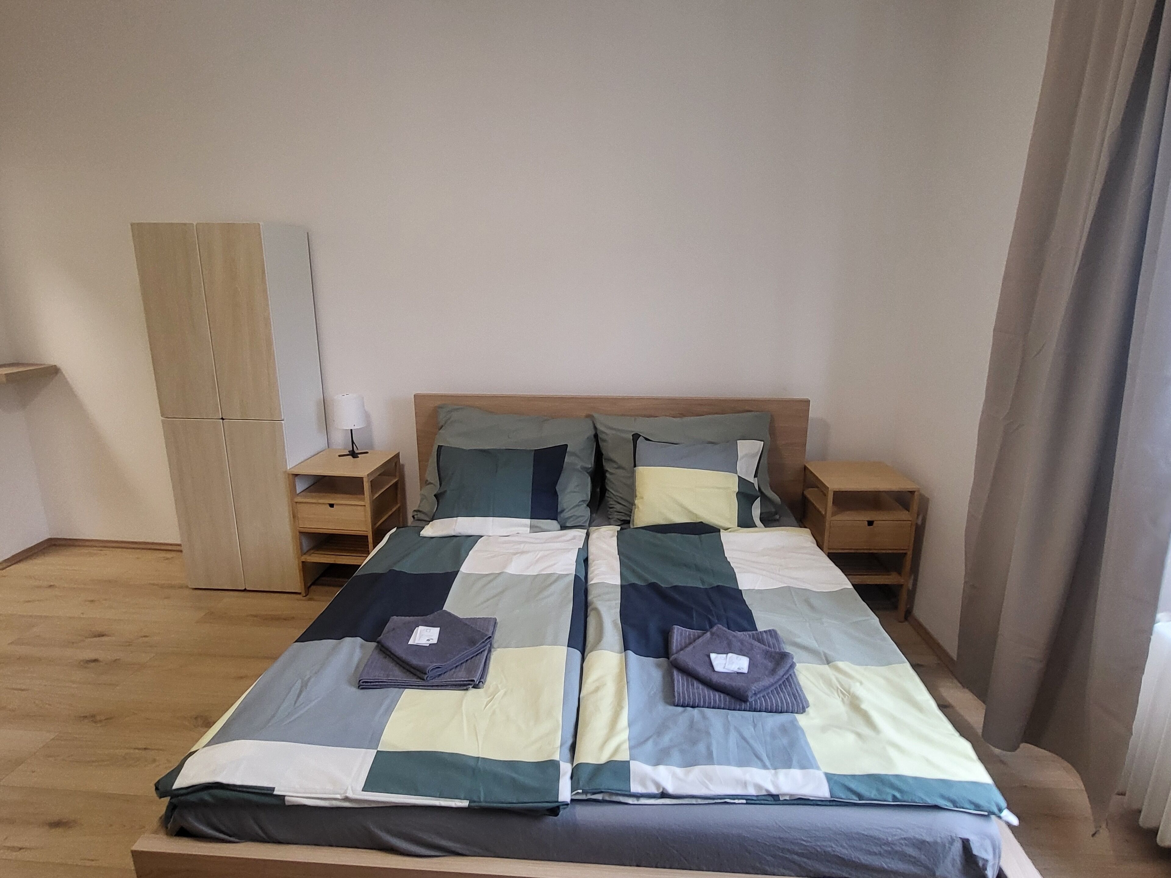 A neatly made bed with a quilt, two bedside tables, a wardrobe, and a lamp.