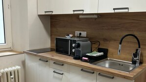 Eine moderne Küche mit weißen Schränken, einer Holz Arbeitsplatte, einer eingebauten Mikrowelle, einem Wasserkocher und einem Spülbecken.